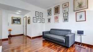Ein Zimmer mit grauem Sofa, Holzboden und gerahmten Kunstwerken an den Wänden.