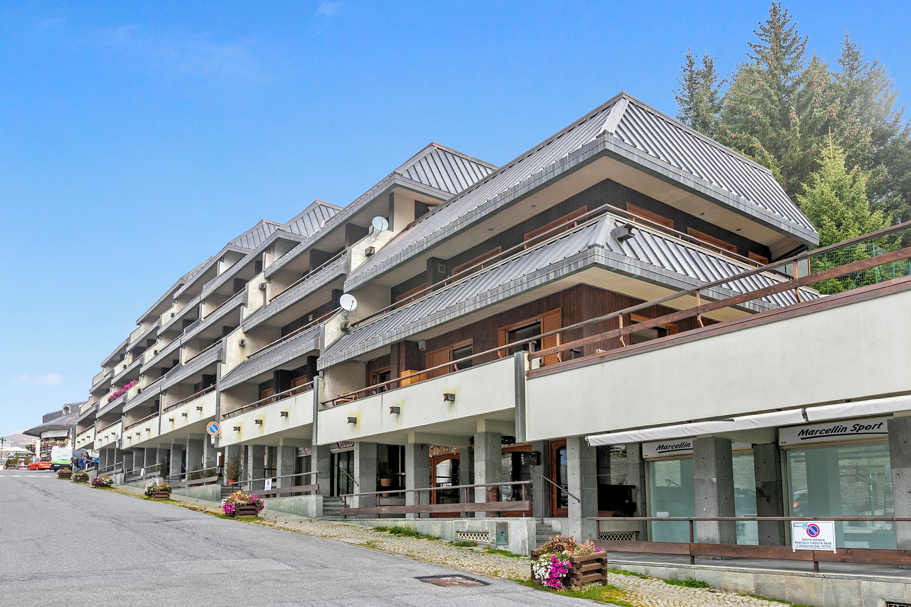 Un hôtel à plusieurs étages doté de balcons, d’un espace extérieur aménagé et d’une enseigne indiquant « Marcellin Sport ».