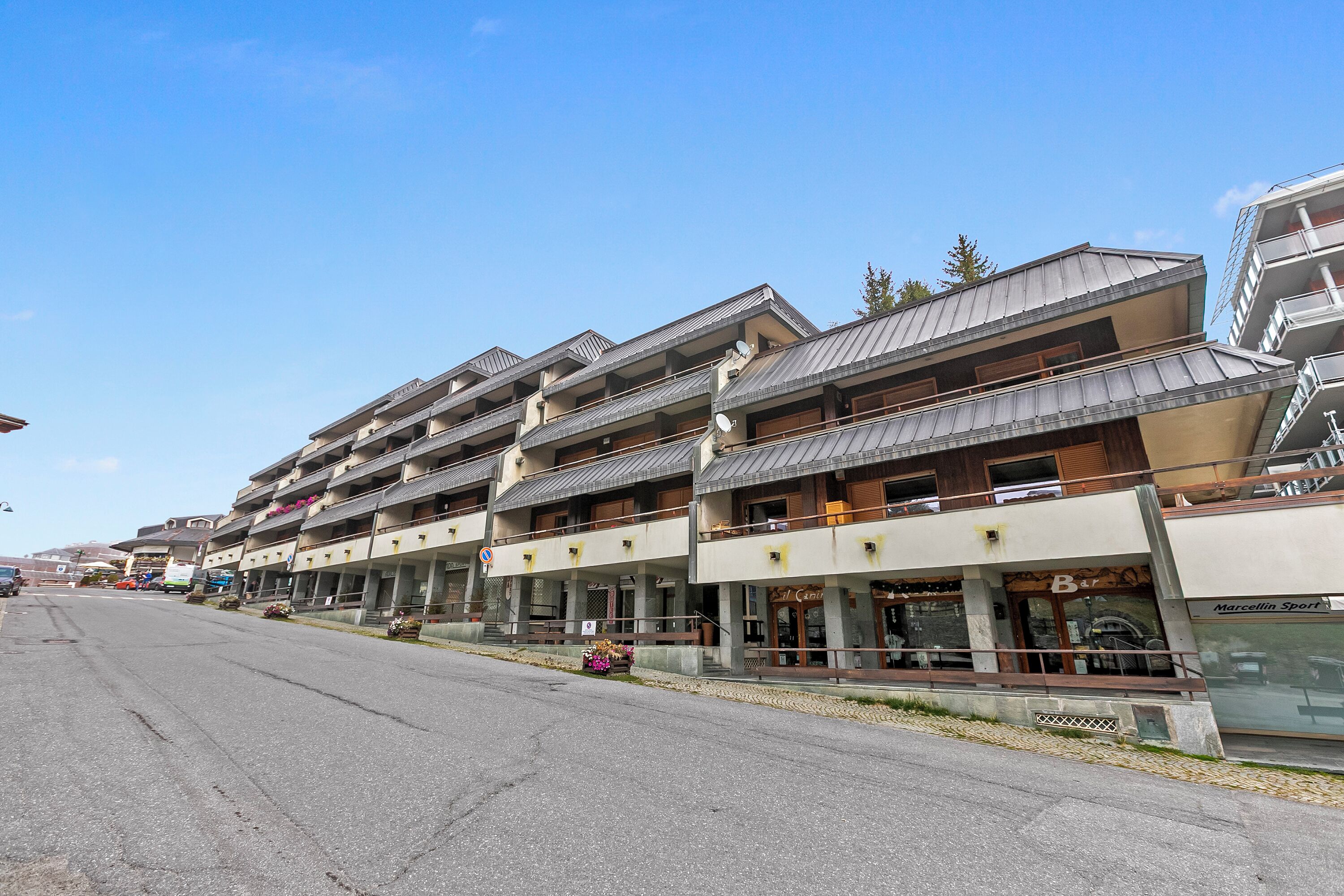 A row of multi-story buildings with balconies, a street in front, and a clear sky.