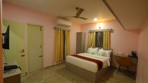 A hotel room with a bed, a desk, a chair, an air conditioning unit, and a ceiling fan. - AG Corporate Stay (Chengalpattu)