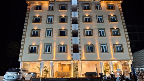 A multi-story hotel with a central vertical light feature, balconies, and a car parked in front. - AG Corporate Stay (Chengalpattu)