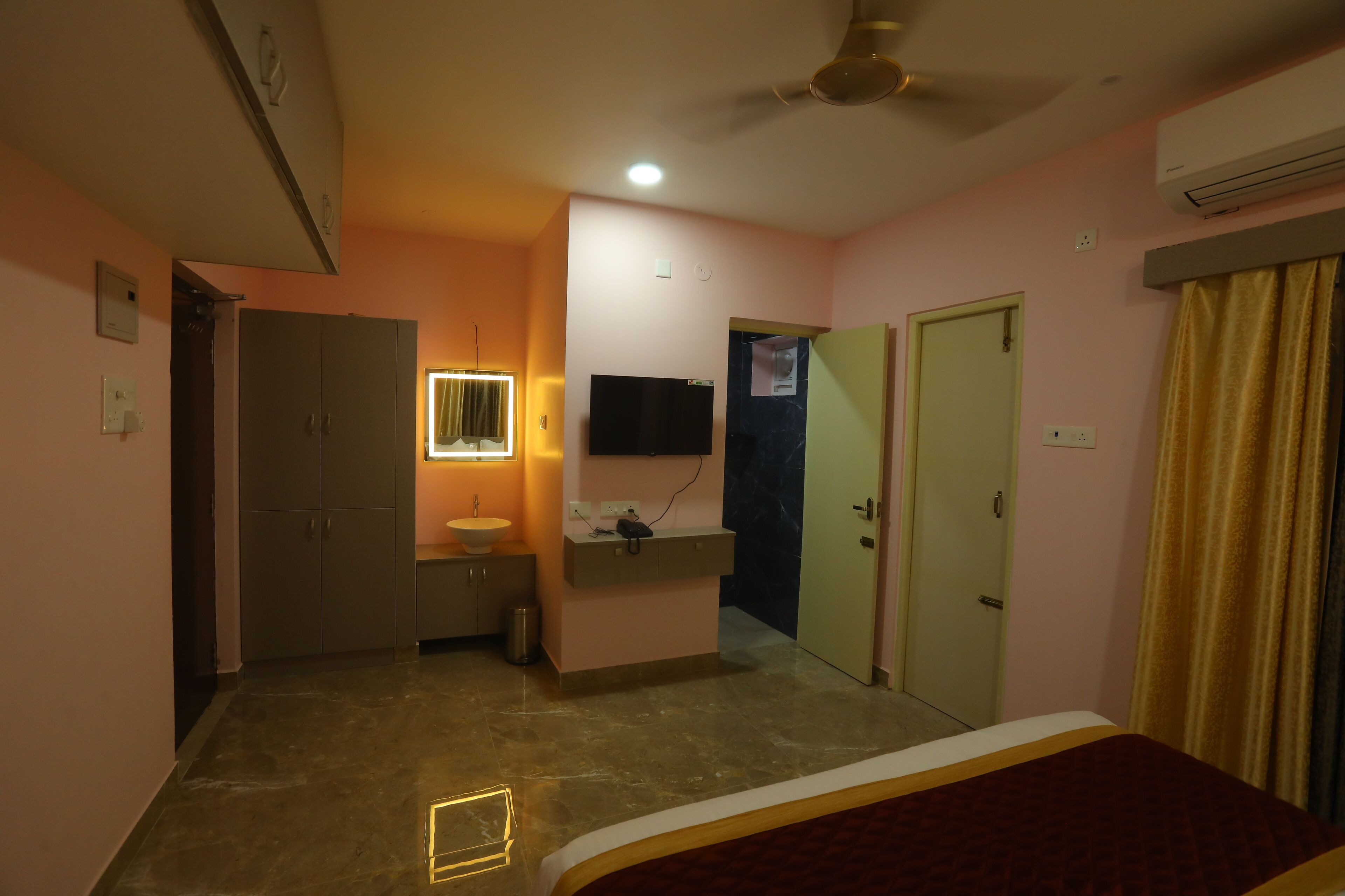 A bedroom with a bed, a vanity with a mirror, a ceiling fan, and a wall-mounted TV.