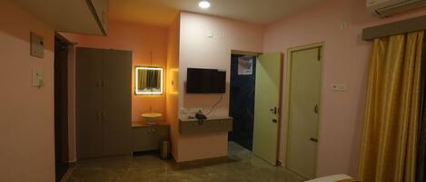 A bedroom with a bed, a vanity with a mirror, a ceiling fan, and a wall-mounted TV.