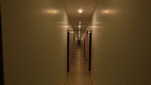 A long, narrow hallway with a series of doors on either side and a light source at the end. - AG Corporate Stay (Chengalpattu)