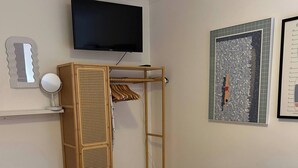 A bedroom with a bed, a TV mounted on the wall, a wooden wardrobe, a mirror, and a framed artwork. - Stylish One Bedroom Apartment in Central Potton (Sandy)