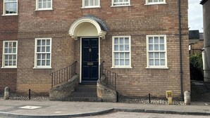 A two-story brick building with a central entrance, multiple windows, and a small staircase leading to the entrance. - Stylish One Bedroom Apartment in Central Potton (Sandy)