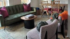 A living room with a green sofa, a patterned armchair, a round coffee table, and a wicker chair. There is a large mirror on the wall and a ceiling light fixture. - Stylish One Bedroom Apartment in Central Potton (Sandy)