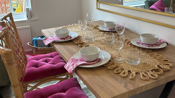 A dining area with a wooden table set for four, including white plates, bowls, and glasses. A wicker basket with a blue towel is on the table. - Stylish One Bedroom Apartment in Central Potton (Sandy)