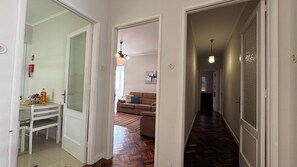 Un couloir avec un plancher en bois, une porte blanche et un canapé marron à l’arrière-plan.