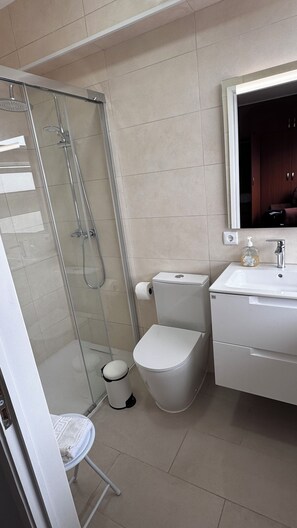 Une salle de bain avec une douche à parois de verre, des toilettes, un lavabo et un miroir.