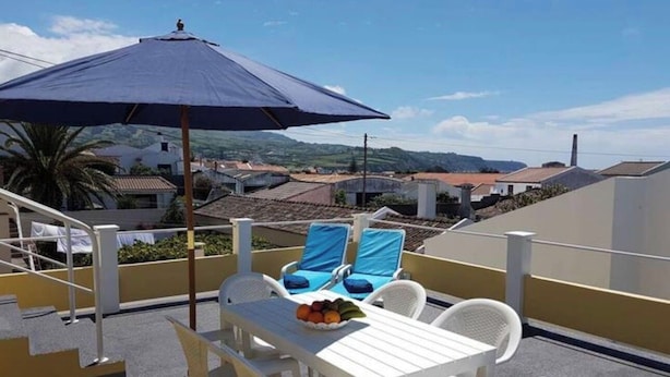 Eine Dachterrasse mit Tisch, Stühlen und einem blauen Sonnenschirm.