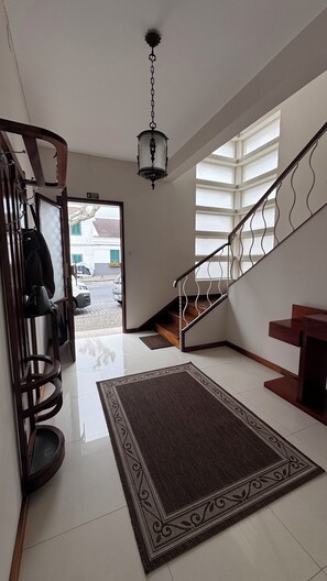 Un hall d’entrée spacieux avec un escalier en bois, un luminaire suspendu et un tapis.