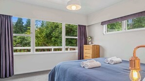 A bedroom with a large bed, a wooden dresser, and a window with curtains. - Tihi Time - Spa Pool, Games Room, Sleeps 10 (Rotorua)