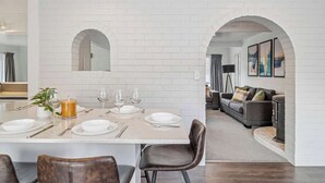 A modern kitchen with white brick walls, an archway leading to a living area with a sofa and a fireplace. - Tihi Time - Spa Pool, Games Room, Sleeps 10 (Rotorua)
