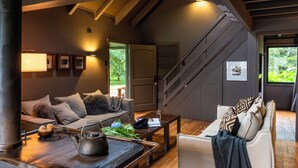 A cozy living room with a sofa, coffee table, and a fireplace. A staircase leads to an upper level. - Parque Cascadas, CABIN Rio Simpson-Patagonia Chile (Aysén)