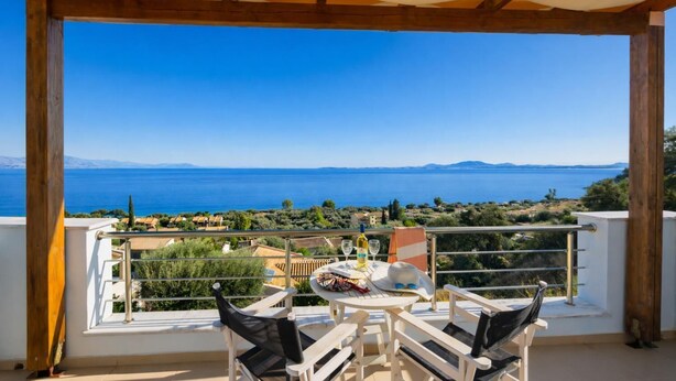 Un balcón con mesa y sillas, con vistas panorámicas al mar y montañas a lo lejos.
