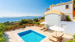 Zona junto a la piscina con vistas al mar, piscina y mobiliario de exterior.