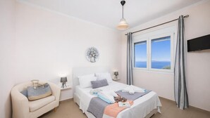 Un dormitorio con cama, mesitas de noche, una silla, televisor y ventana con vistas.