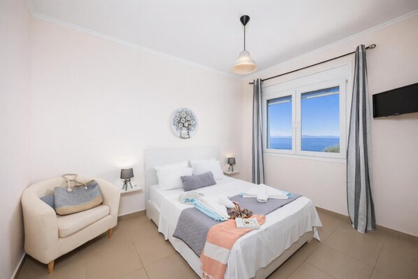 A bedroom with a bed, bedside tables, a chair, a TV, and a window with a view. - Villa Alya View - Three Bedroom Villa, Sleeps 6 (Mparmpati)