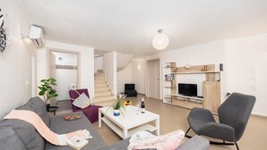 Una sala de estar moderna con un sofá gris, un sillón púrpura, una mesa de centro blanca y un televisor sobre un mueble de madera.