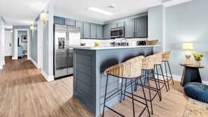 Cocina moderna con gabinetes grises, electrodomésticos de acero inoxidable y una isla central con taburetes.