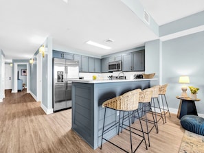 A modern kitchen with grey cabinets, stainless steel appliances, and a central island with bar stools. - 🏖️Endless Gulf Views-Next To Pier Park-Pools-Hot Tubs-Calypso 3-2003 - Sunset Bl (Panama City Beach)