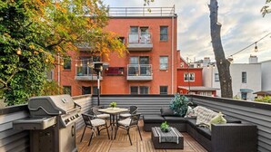 En tagterrasse med grill, siddepladser og udsigt til en rød murstensbygning.