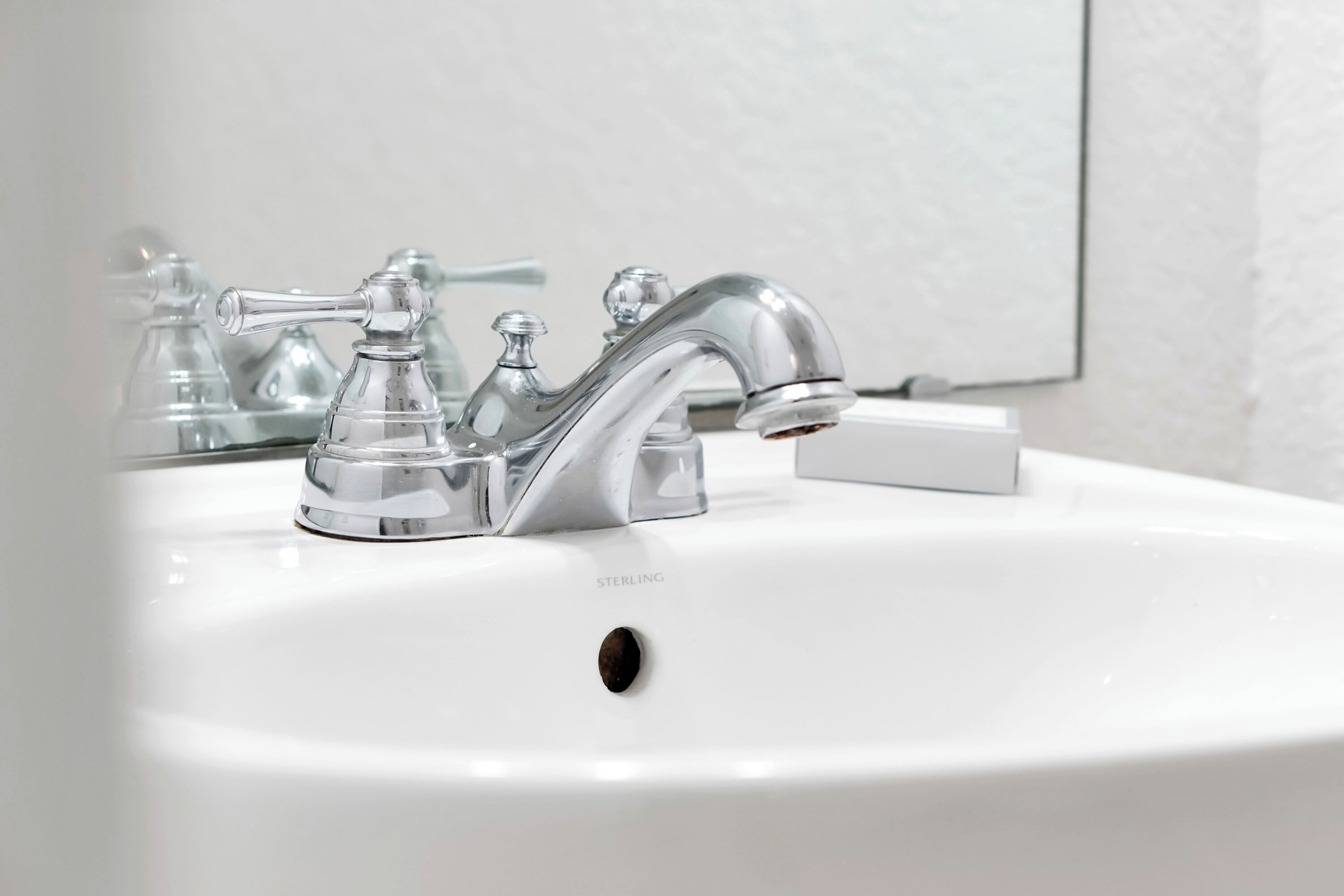 Un lavabo blanc dans une salle de bain, doté d'un robinet moderne et d'un miroir au-dessus.