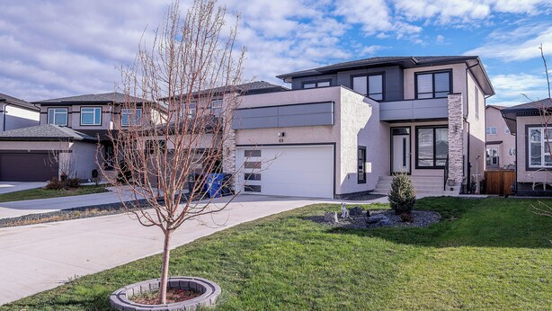 Ein modernes, zweistöckiges Haus mit Garage, gepflegtem Rasen und einem kleinen Baum im Vorgarten.