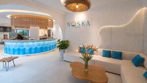 A modern hotel lobby with a reception desk, a seating area with a sofa and coffee table, and a large wall-mounted sign. - Noska Hotel (Phu Quoc)
