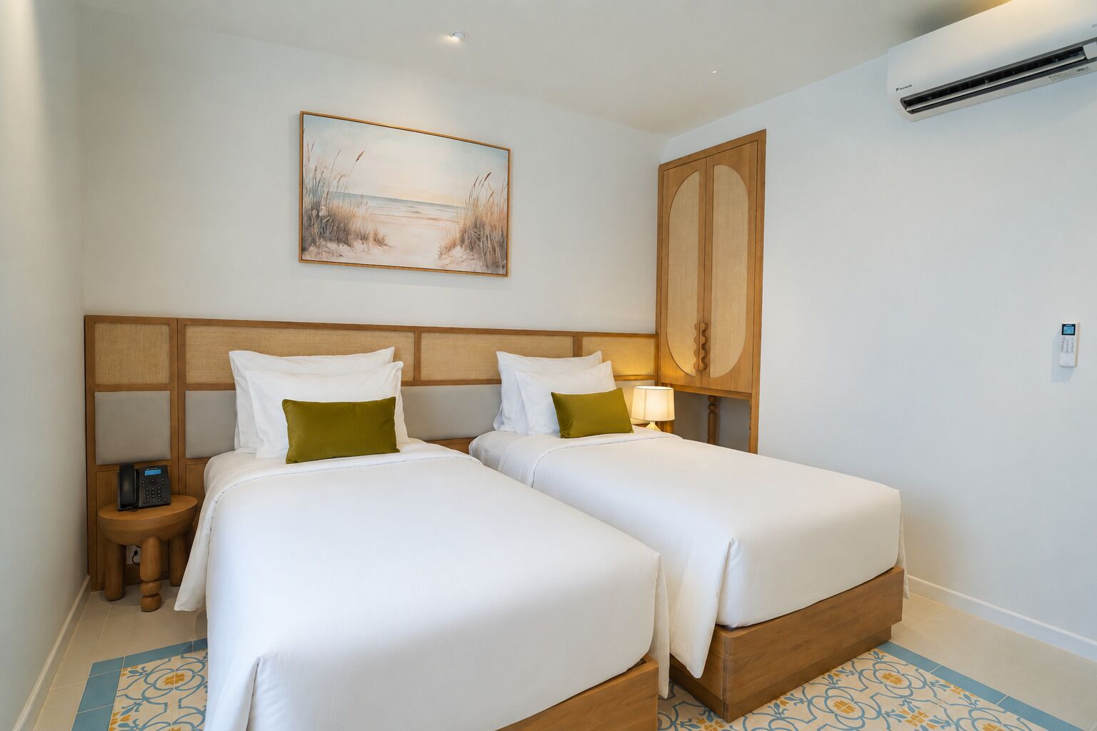 A hotel room with two beds, a painting, an air conditioning unit, and a bedside table with a phone.