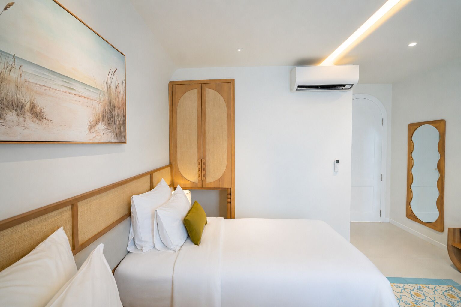 A hotel room with a bed, a painting, an air conditioning unit, and a door.