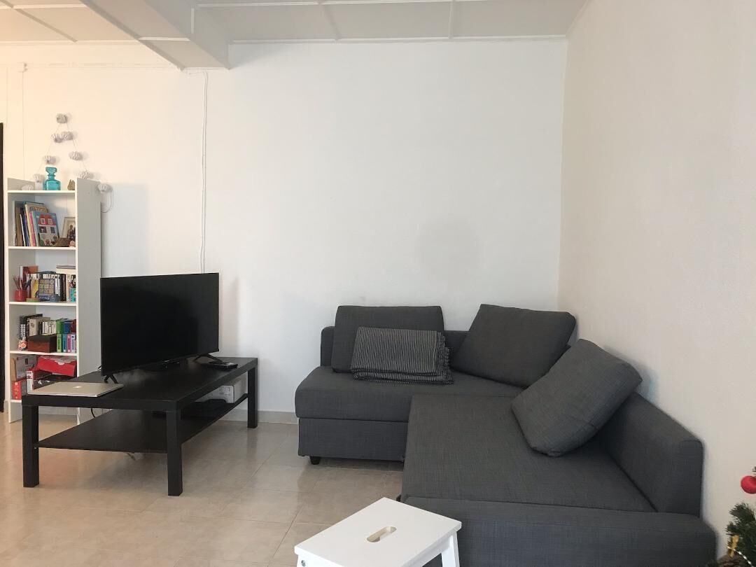 Ein Wohnzimmer mit einem dunkelgrauen Sofa, einem schwarzen Fernseher auf einem Standfuß und einem weißen Beistelltisch.