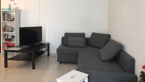 Una sala de estar con un sofá gris oscuro, un televisor negro sobre un mueble bajo y una mesita auxiliar blanca.