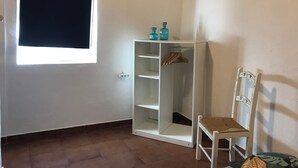 Una habitación con un armario blanco, una silla de madera y una ventana con persiana negra.
