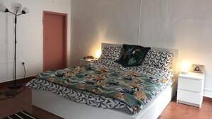 Un dormitorio con cama, mesita de noche, lámpara de pie y una puerta.