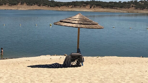 Una playa con un paraguas de paja y una silla a rayas.