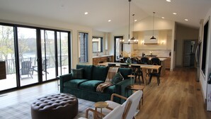 A spacious living area with a green sofa, ottoman, and modern chairs, a dining area with a wooden table, and a kitchen with pendant lighting. - Amazing 6-bedroom Lakefront Home in Cassopolis, MI (Cassopolis)