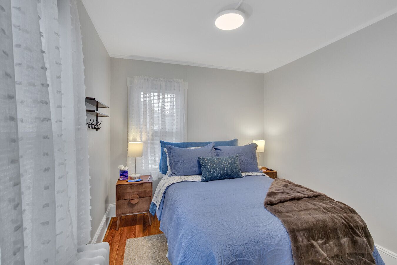 Une chambre à coucher avec un lit, des tables de chevet, une fenêtre avec des rideaux légers et un luminaire au plafond.