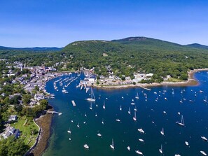 An aerial view of a coastal town with a marina filled with boats, surrounded by green hills and residential buildings. - Historic Condo in Downtown Camden, steps to Harbor (Camden)