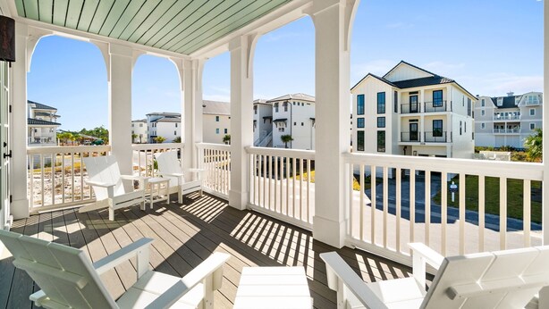 Una terrazza esterna coperta con ringhiere bianche e posti a sedere, con vista su una zona residenziale con case moderne.