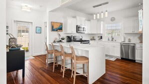Una cucina moderna con mobili bianchi, una grande isola con sgabelli da bar, un forno a microonde e una lavastoviglie.