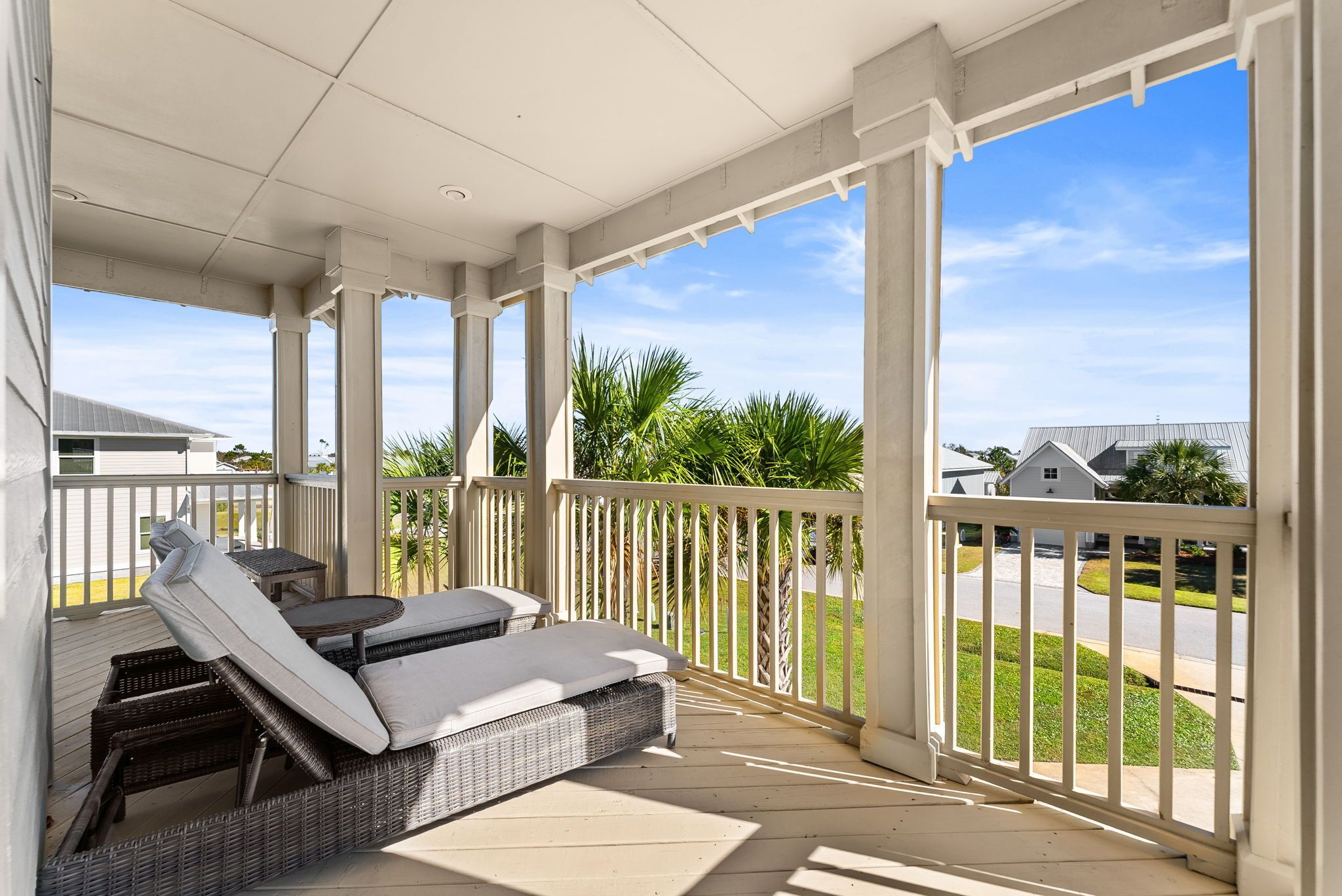 A covered outdoor seating area with wicker furniture and a view of a residential neighborhood.