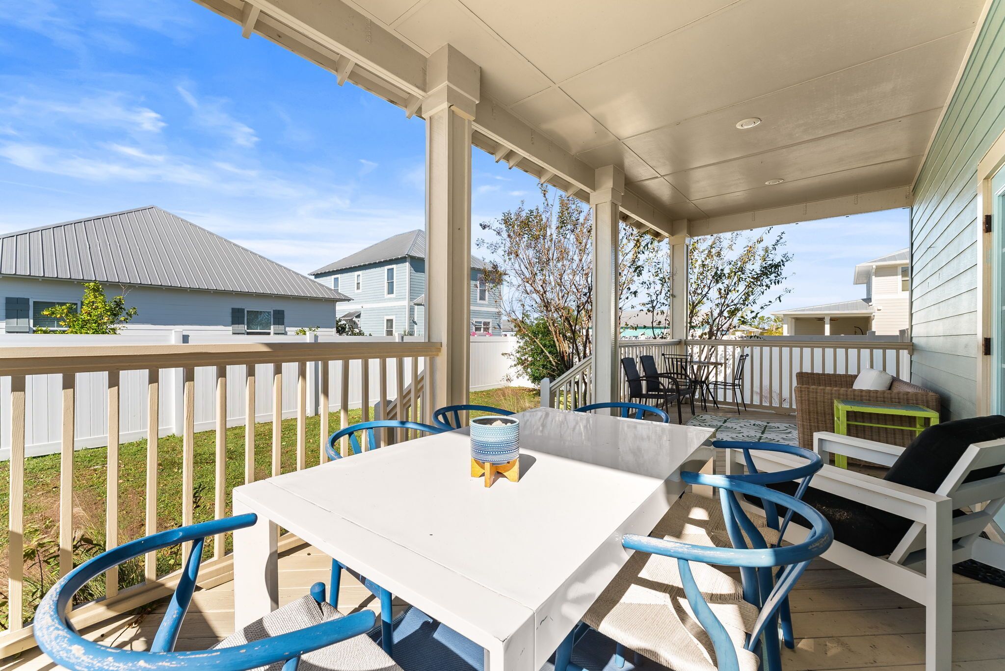 A covered patio area with a white table and blue chairs, a wicker sofa, and a small green stool.