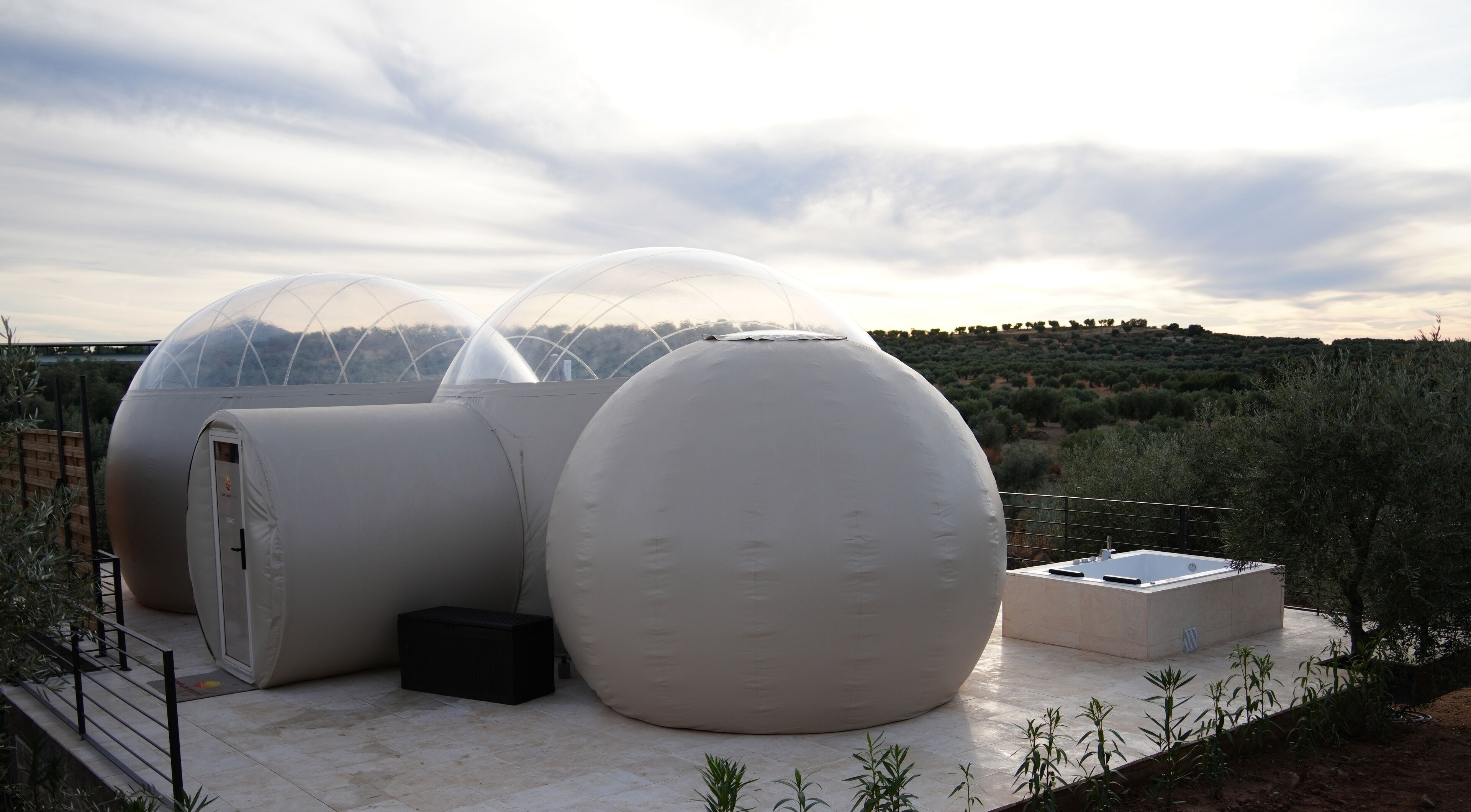 Two spherical structures with transparent domes, a small black box, and a rectangular sink on a tiled platform with a view of a hilly landscape.