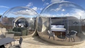 Two transparent dome structures with furniture inside, including a sofa, chairs, and a bed. - Panoramic Suites (Guadamur)