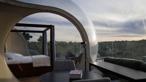 A modern, dome-shaped room with a bed, seating area, and a view of the outdoors. - Panoramic Suites (Guadamur)