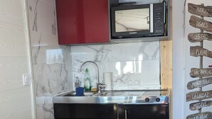Une cuisine de taille réduite avec des placards rouges, un micro-ondes noir et une table en bois.