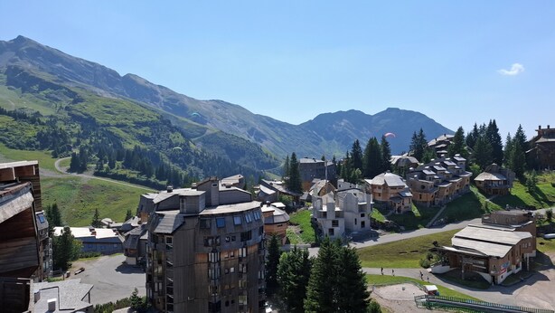 Un village de montagne aux bâtiments traditionnels en bois, avec une route sinueuse et un ciel dégagé.