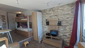 Une petite pièce avec des lits superposés, un bureau en bois, un ordinateur et un téléviseur.